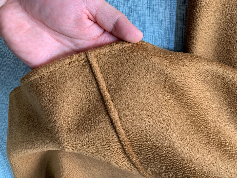 A hand holding a brown garment edge at a seam junction