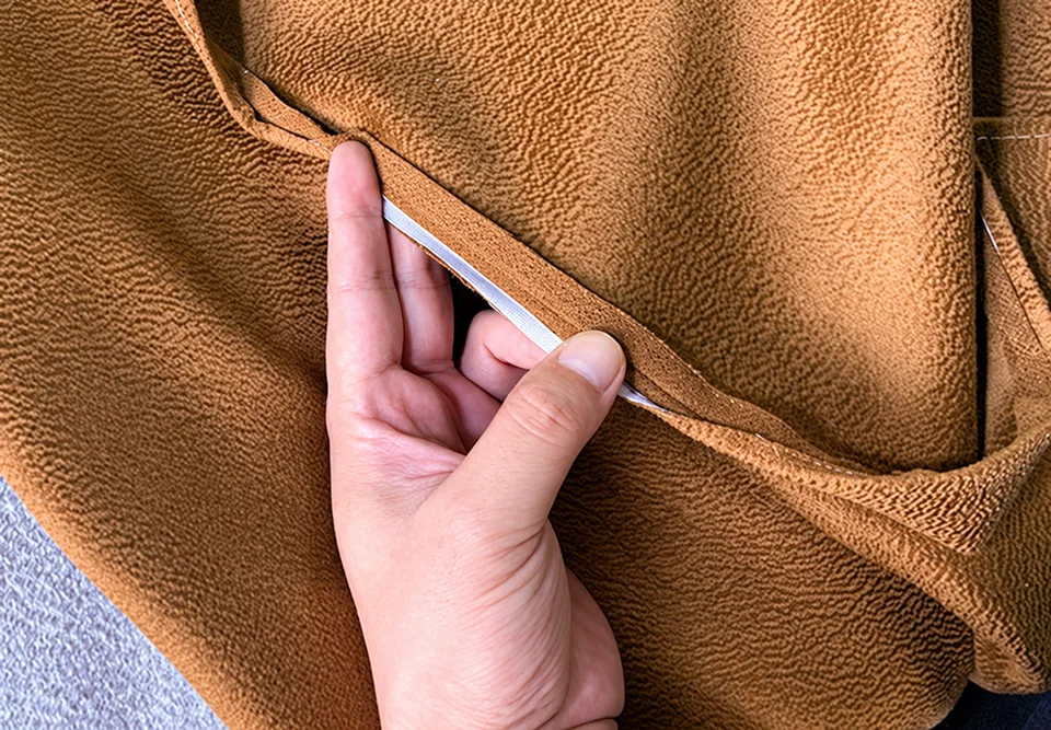 A hand opening a brown fabric edge to reveal a pale narrow strip inside