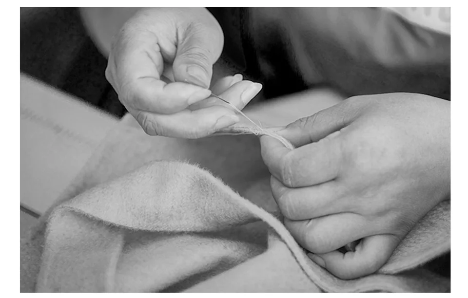 Black-and-white close-up of hands guiding a needle through a fabric edge