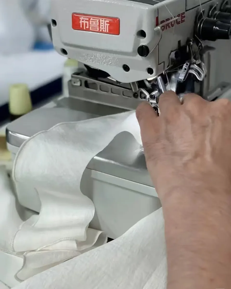 A hand guiding light-coloured fabric beneath an industrial sewing machine