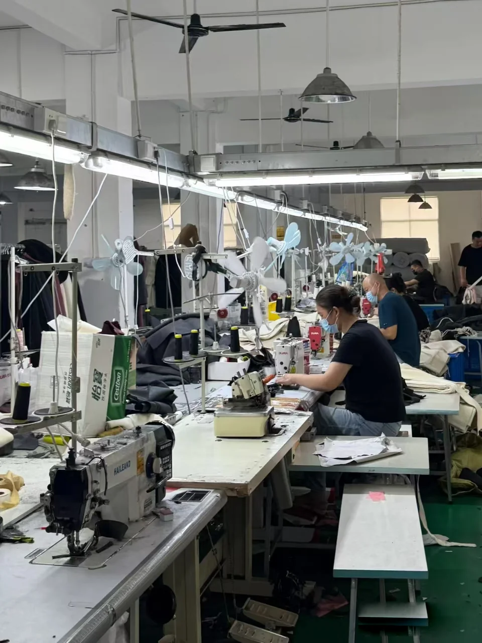 People working at sewing stations with fabric pieces and garments nearby